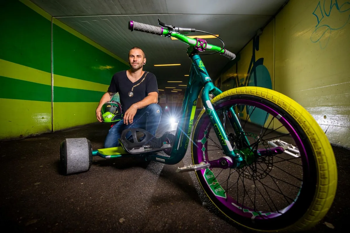 Ein Mann kniet hinter seinem Drift Trike.